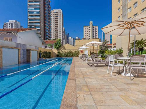 einen Pool mit Tischen, Stühlen und einem Sonnenschirm in der Unterkunft Mercure Sao Paulo Vila Olimpia in São Paulo
