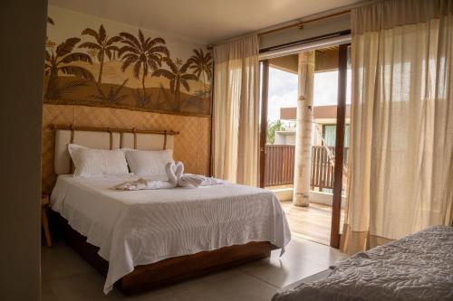 a bedroom with a bed with white sheets and a balcony at Casa com Ofurô, Piscina Aquecida e Cozinheira in Barra do Camaragibe