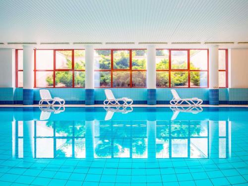 a swimming pool with two chairs and windows at Mercure Jelenia Góra in Jelenia Góra