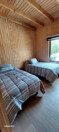 two beds in a wooden room with a window at Casa de campo chiloe pugueñun ancud in Ancud