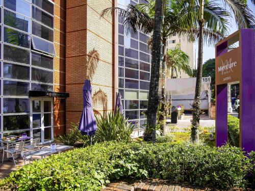 a building with a table and chairs and palm trees at Mercure Sao Paulo Jardins in Sao Paulo