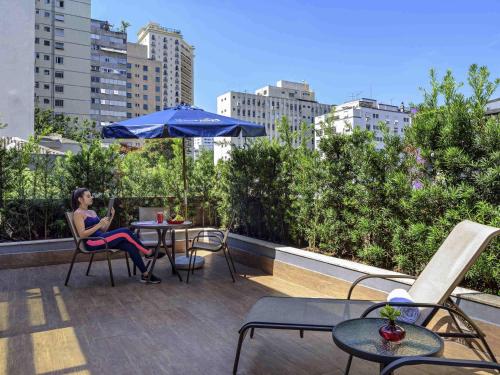 eine Frau, die mit einem Sonnenschirm an einem Tisch auf einem Dach sitzt in der Unterkunft Mercure Sao Paulo Jardins in São Paulo