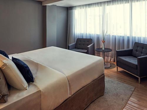 ein Schlafzimmer mit einem großen Bett und zwei Stühlen in der Unterkunft Grand Mercure Brasilia Eixo Monumental in Brasilia