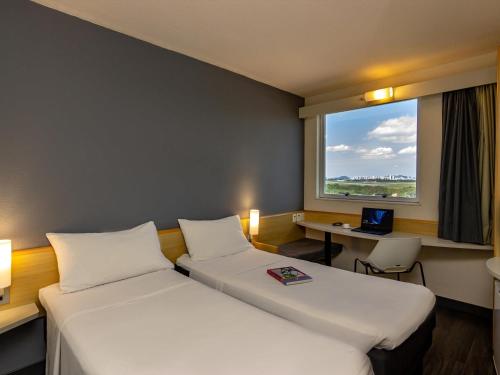a room with two beds and a desk with a window at ibis Vitoria Aeroporto in Vitória