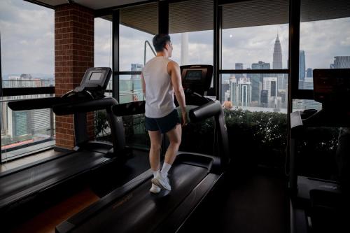 a man on a treadmill in a gym looking out the window at Ceylonz Suites KLCC Rooftop Infinity Pool KL Tower View in Kuala Lumpur