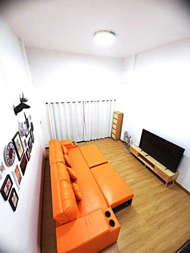 a living room with an orange couch and a flat screen tv at A Day Home in Chiang Mai