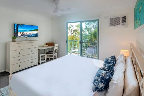 a bedroom with a large white bed with a desk and a window at Sunset Waters 12 on Hamilton Island by HamoRent in Hamilton Island