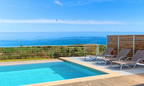 a swimming pool with two chairs and the ocean at Vista Mare Villa Beheizter Pool in Georgioupoli