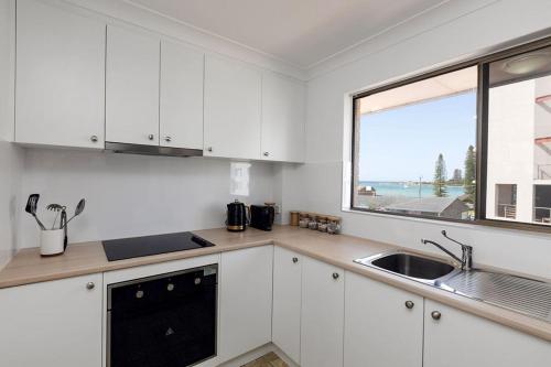 une cuisine avec des armoires blanches, un évier et une fenêtre dans l'établissement Del Boca Vista Tuncurry, à Tuncurry