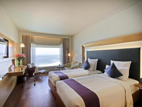 ein Hotelzimmer mit zwei Betten und einem Schreibtisch in der Unterkunft Novotel Visakhapatnam Varun Beach in Visakhapatnam