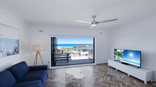 a living room with a blue couch and a flat screen tv at Elanora 3 - Beachfront Unit With Views! in Avoca Beach