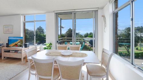 a dining room with a white table and chairs and windows at Seaview 7 - Prime Position Beachside Holiday in Avoca Beach