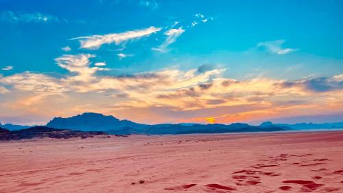 a beach with footprints in the sand with a sunset at Wadi Rum Desert Life in Wadi Rum