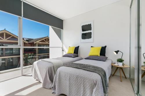 two beds in a bedroom with a large window at Ultra modern 2 bdrm in St Leonards Crows Nest - 803NOR in Sydney