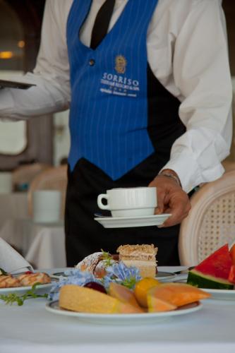 um homem de colete azul segurando um prato de comida em Sorriso Thermae Resort & Spa em Ischia