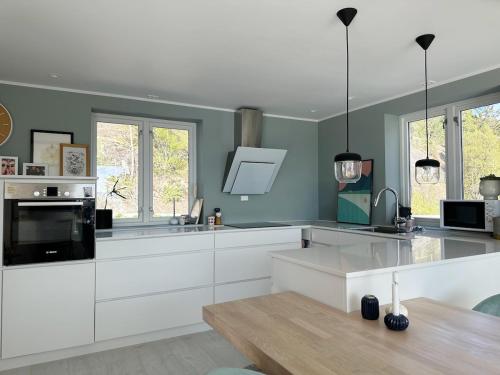 eine Küche mit weißen Schränken, einem Tisch und Fenstern in der Unterkunft Lovely sea view in modern family house! in Steinkjer
