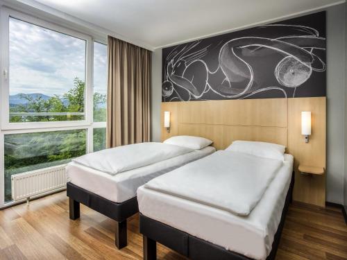 two beds in a room with a large window at ibis Wörthersee in Pörtschach am Wörthersee