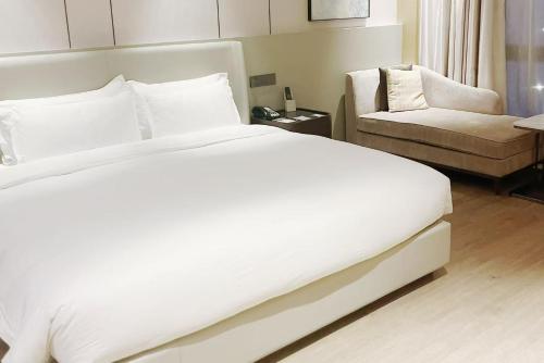 um quarto com uma grande cama branca e uma cadeira em Wyndham Shanghai Pudong em Xangai