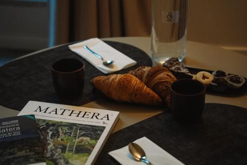 une table avec une assiette de pain, des tasses et un magazine dans l'établissement CA' DO' Guest House, à Matera