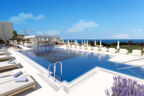 Una piscina con sillas y el océano al fondo. en Amare Beach Hotel Sancti Petri - Adults Recommended, en Chiclana de la Frontera