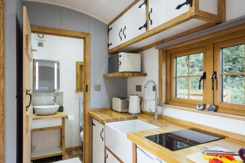a kitchen with white counters and wooden cabinets at Cwtch Ffynnone Luxury Shepherds Hut in Newchapel