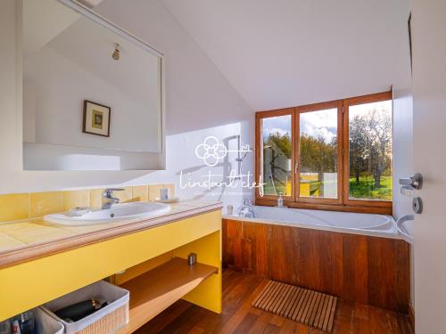 ein Badezimmer mit Badewanne und Waschbecken und einem Fenster in der Unterkunft Bulle de calme bucolique - jardin & piscine privée in Fercé-sur-Sarthe