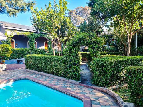 a swimming pool in front of a house with bushes at Hobbit Boutique Hotel in Bloemfontein