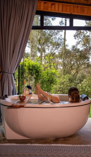 a woman laying in a bathtub in front of a window at Refúgio na Serra com Banheira e Belo Nascer do Sol in Rio Rufino