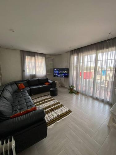 een woonkamer met een zwarte bank en een televisie bij Appartement Boulimat Bejaia in Matriouene