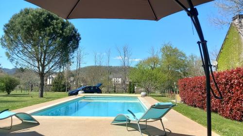 ein Swimmingpool mit zwei Stühlen und einem Sonnenschirm in der Unterkunft Maison tout confort avec piscine chauffée au bord des rives de la Dordogne in Argentat