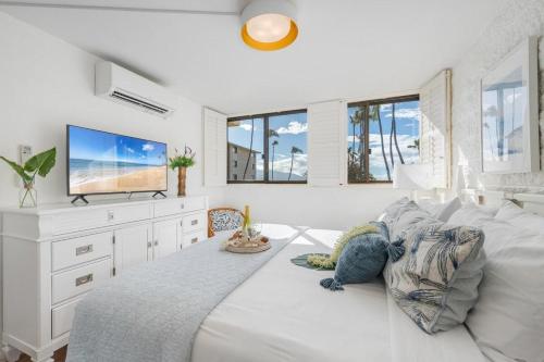 een witte slaapkamer met een groot bed en een flatscreen-tv bij Kanai A Nalu 211 · KAN 211 Remodeled OceanFront 2BD for Whale Wa in Wailuku