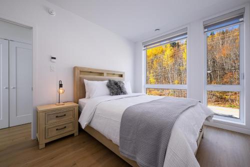 a white bedroom with a bed and two windows at Panorama 1253: Two-Level Sanctuary & Views in Petite-Rivière-Saint-François