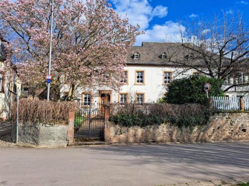 une maison blanche avec une clôture et des arbres à fleurs dans l'établissement Ferienwohnung Mit Garten Und Parkplatz, à Neumagen-Dhron