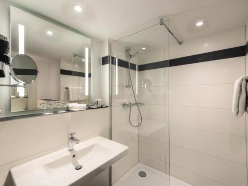 a white bathroom with a sink and a shower at Mercure Hotel Mannheim am Friedensplatz in Mannheim