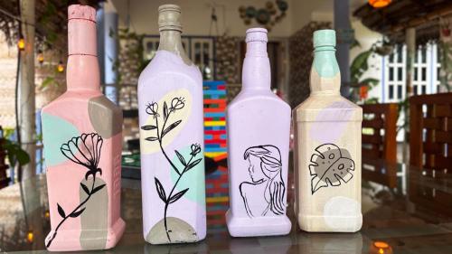 quatre bouteilles avec des fleurs peintes dessus posées sur une table dans l'établissement Hideaway villa, à Varkala