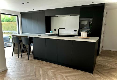 eine Küche mit schwarzen Schränken und einer Theke mit Stühlen in der Unterkunft Vakantiewoning rand Brugge in Jabbeke