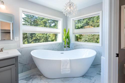 a white tub in a bathroom with two windows at Sopra Bella- 4 bedroom home in Corvallis