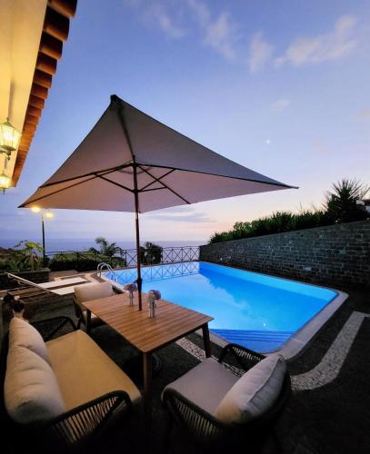 ein Tisch mit Sonnenschirm neben einem Swimmingpool in der Unterkunft Villa Ocean Wave Calheta - Oversized Pool & Stunning Ocean Views in Calheta