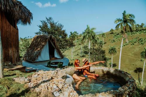 Zwei Frauen sitzen in einer Wasserlache vor einem Zelt in der Unterkunft OYA New Earth Luxury Romantic Glamping with Private Outdoor Bath in Jamao al Norte