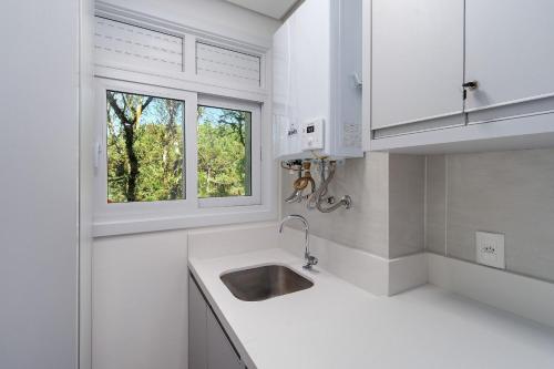 Una cocina blanca con fregadero y ventana. en Vêneto Luxo 1 dorm Achei Gramado, en Gramado