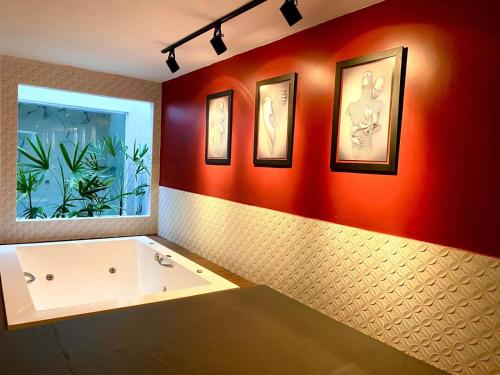a bathroom with a white tub and a red wall at Blue Suítes - motel in Cascavel