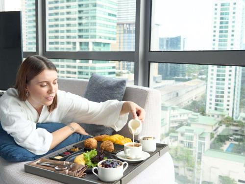 a woman sitting on a couch with a tray of food at Novotel Suites Manila at Acqua in Manila