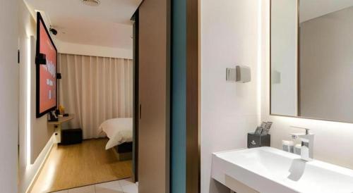 Un baño con lavabo y espejo y un dormitorio. en Magnotel Ningbo Tianyi Plaza Railway Station, en Ningbo