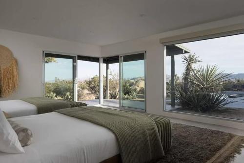 - une chambre blanche avec 2 lits et de grandes fenêtres dans l'établissement Luxury Villa Pool & Spa Looking Glass, à Yucca Valley
