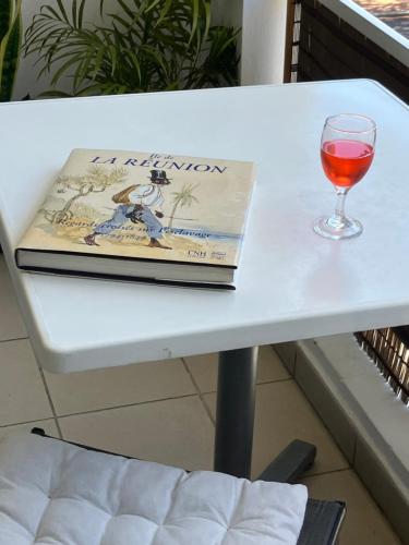 un libro y una copa de vino en una mesa en L'Échappée Bleue Studio à 5 min du port et plage, en Saint-Gilles-les-Bains