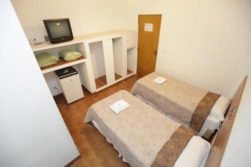 a small room with two beds and a television at Hotel Pouso Novo in Matão