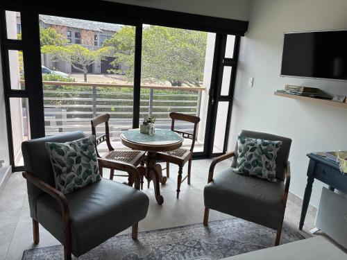 een woonkamer met een tafel, stoelen en een televisie bij Topiary Lux Studio 16! in Herolds Bay
