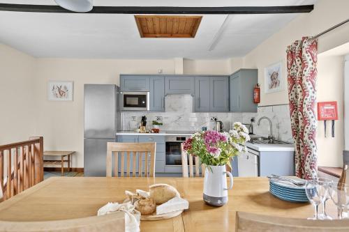 a kitchen with blue cabinets and a wooden table with flowers at Cherry Cottage in Saint Endellion