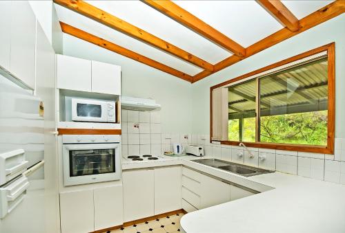 a kitchen with white cabinets and a large window at Acclaim Pine Grove Holiday Park in Esperance