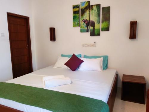 a bedroom with a white bed with paintings on the wall at Bienvenido Cozy Madiha in Matara
